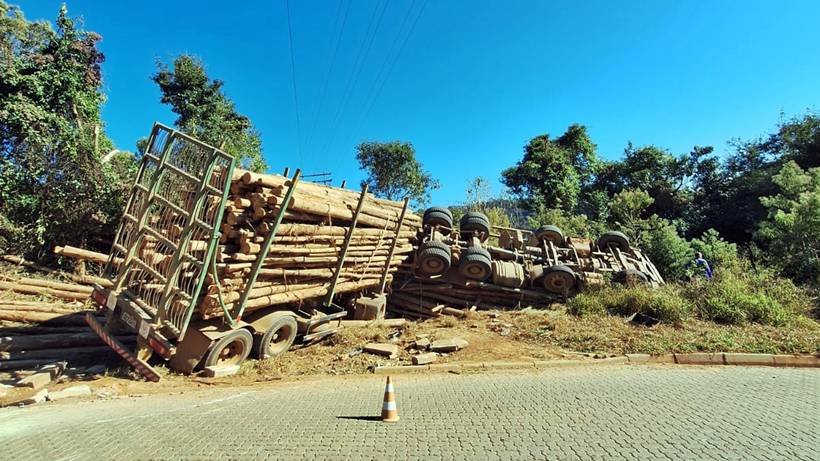 Carreta com madeira tomba em estrada rural e motorista fica preso às ferragens