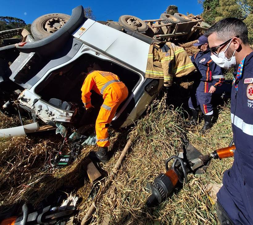 Carreta com madeira tomba em estrada rural e motorista fica preso às ferragens